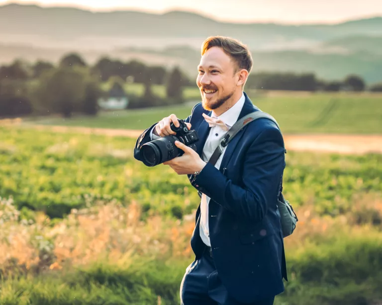 Professioneller Hochzeitsfotograf bei einem Outdoor-Shooting in Bad Neuenahr-Ahrweiler, lächelnd mit Kamera, bereit, unvergessliche Momente festzuhalten.